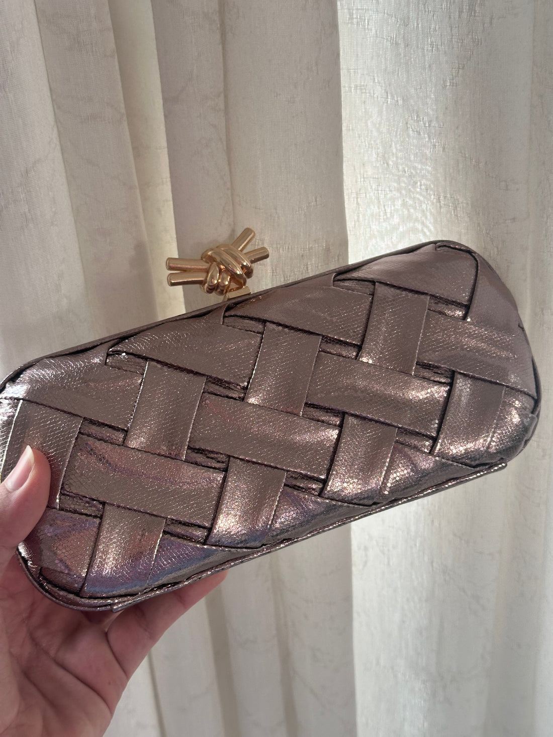 Metallic woven clutch held in front of a white curtain