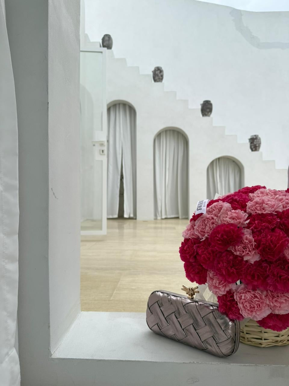 Silver clutch and pink flowers on a white surface with a blurred architectural background