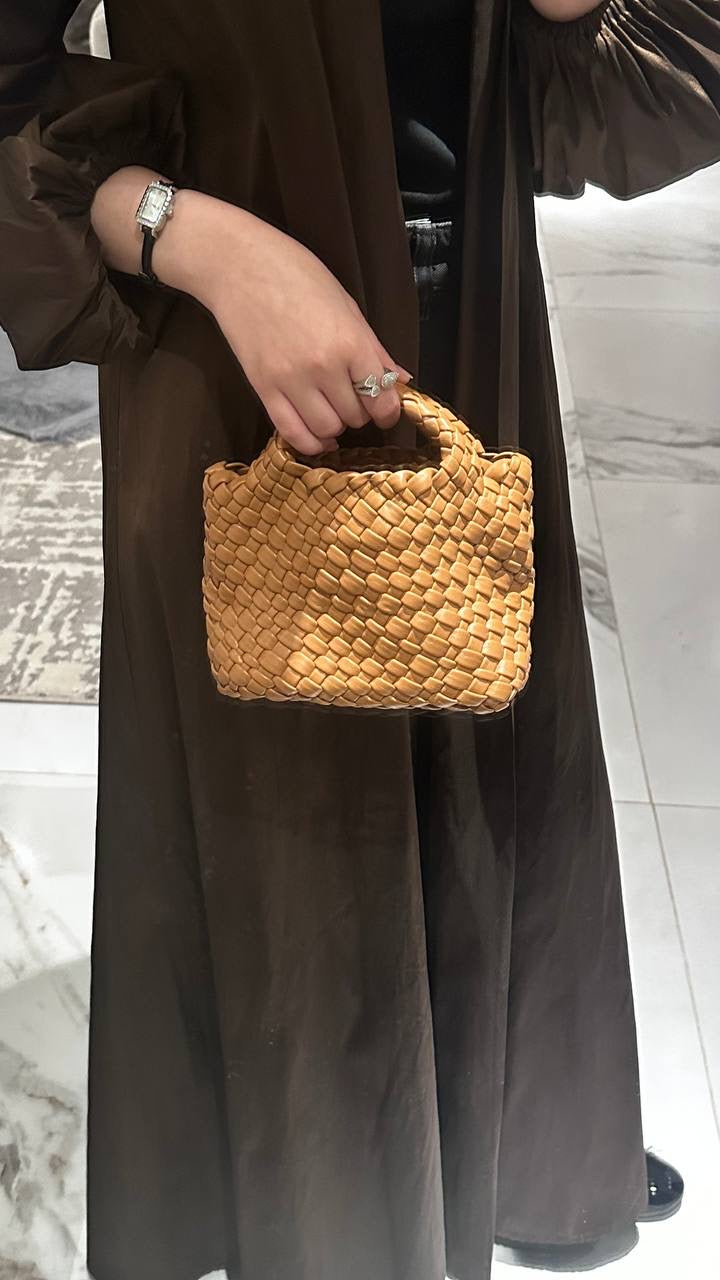 A person holding a brown, textured vegan leather handbag with a detachable shoulder strap.