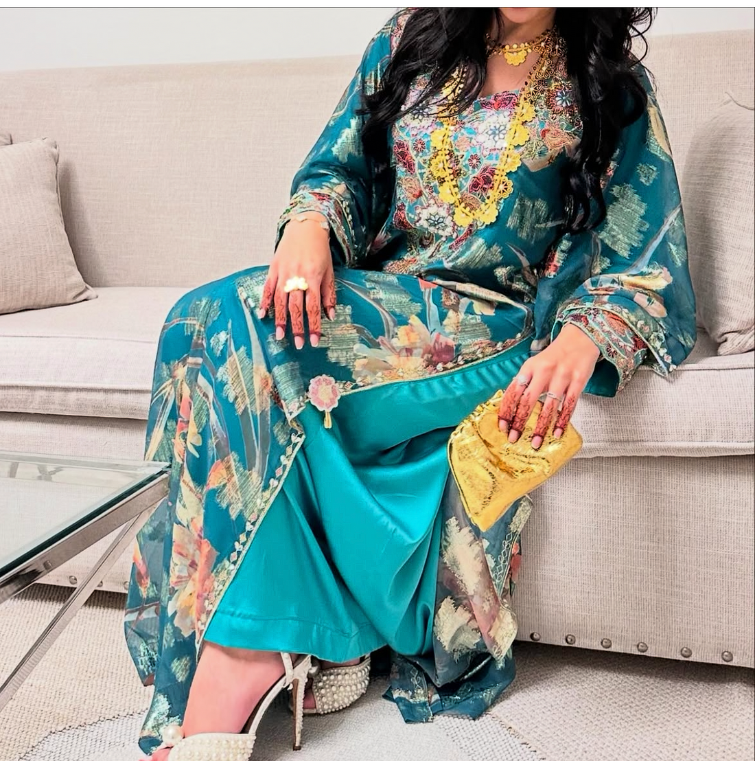 Woman in a colorful traditional outfit with a yellow clutch sitting on a couch.