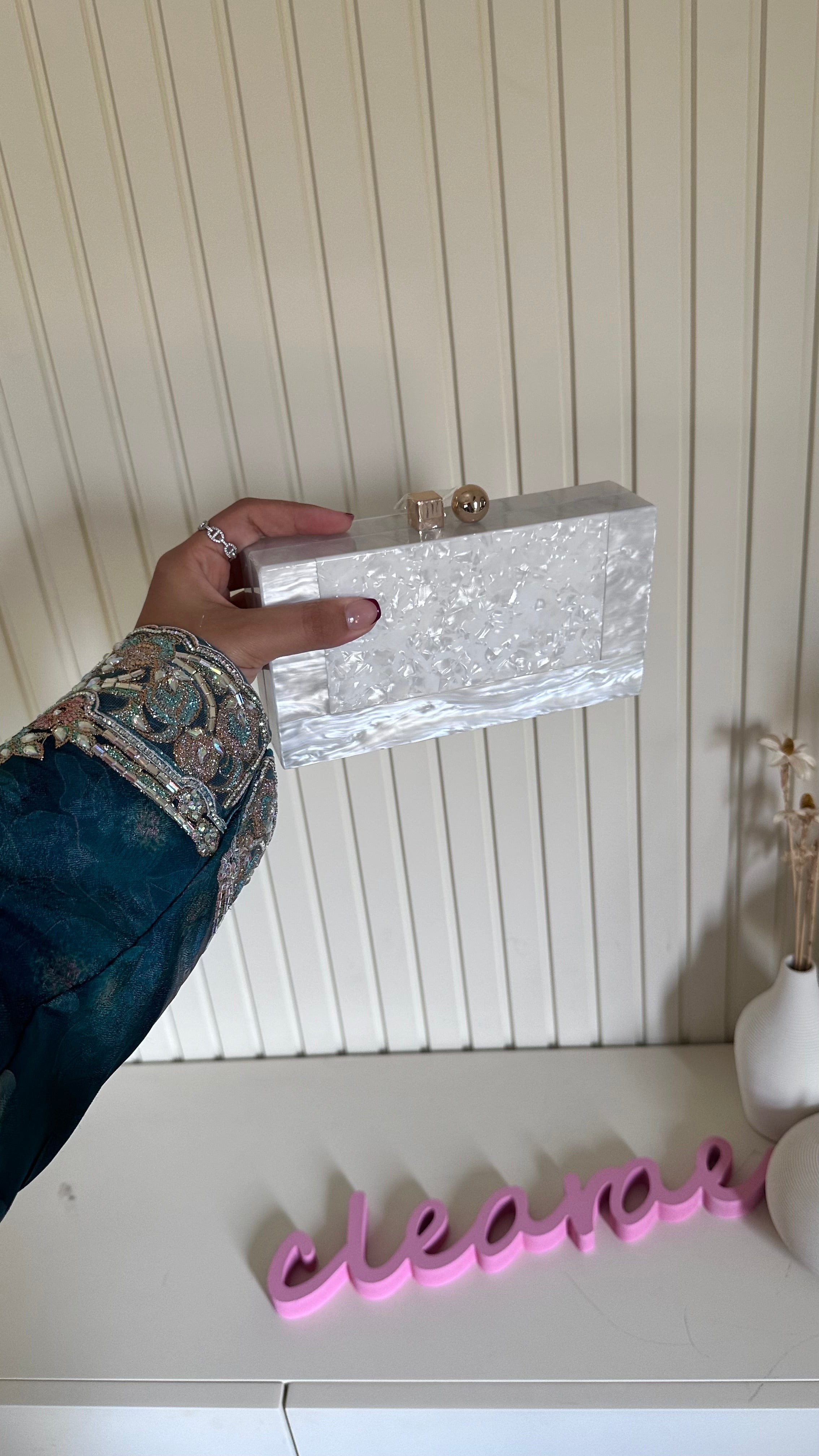 Hand holding a silver clutch with decorative embellishments against a white background.