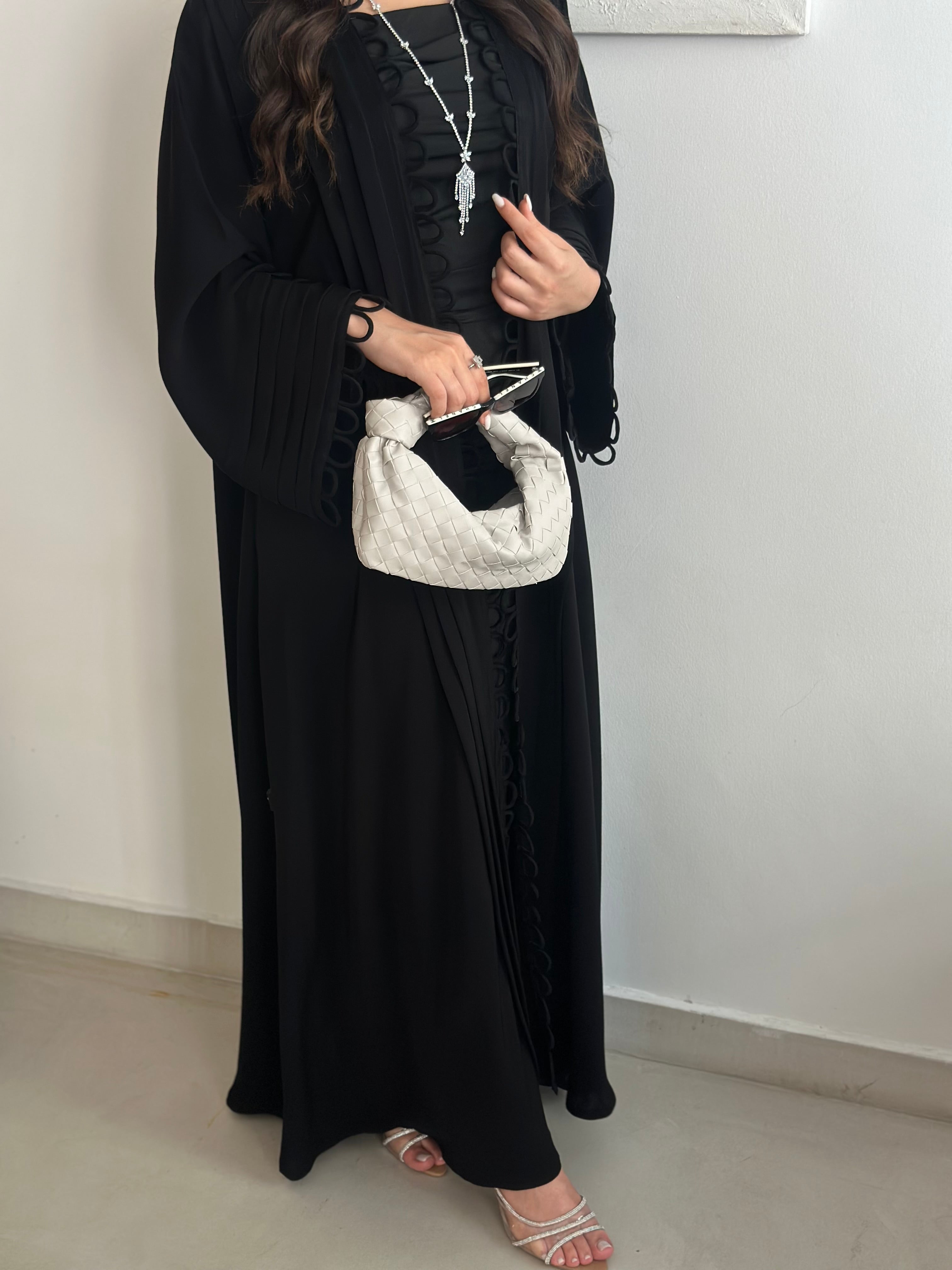 Person wearing a black outfit holding a white handbag against a plain background