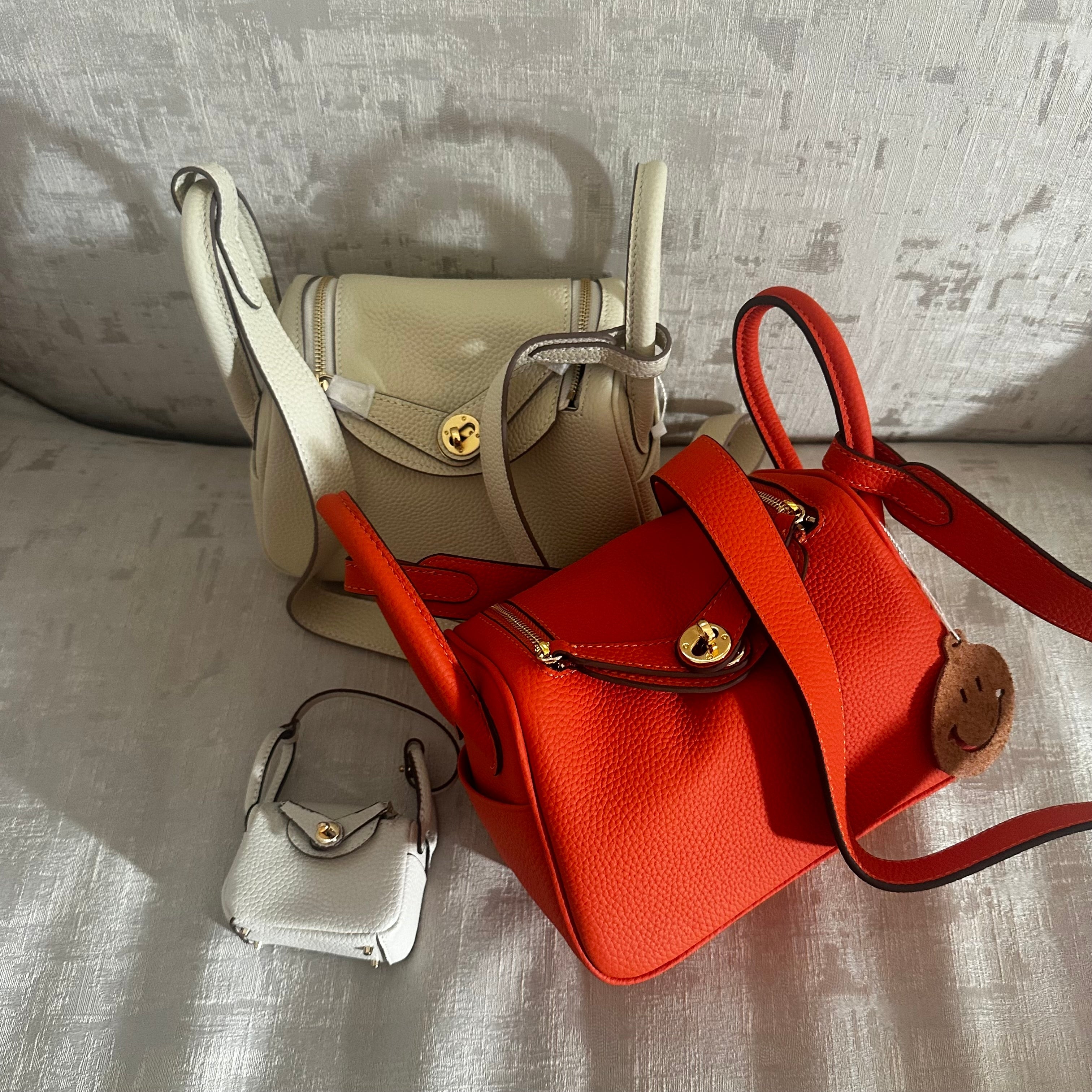 This image displays a collection of three stylish handbags in varying colors and designs, laid out on a textured surface. The smallest bag is a compact white purse with a zipper and a detachable strap, ideal for carrying essentials.