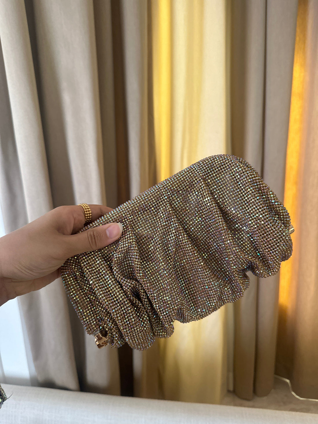 Hand holding a sparkling clutch against a curtain background