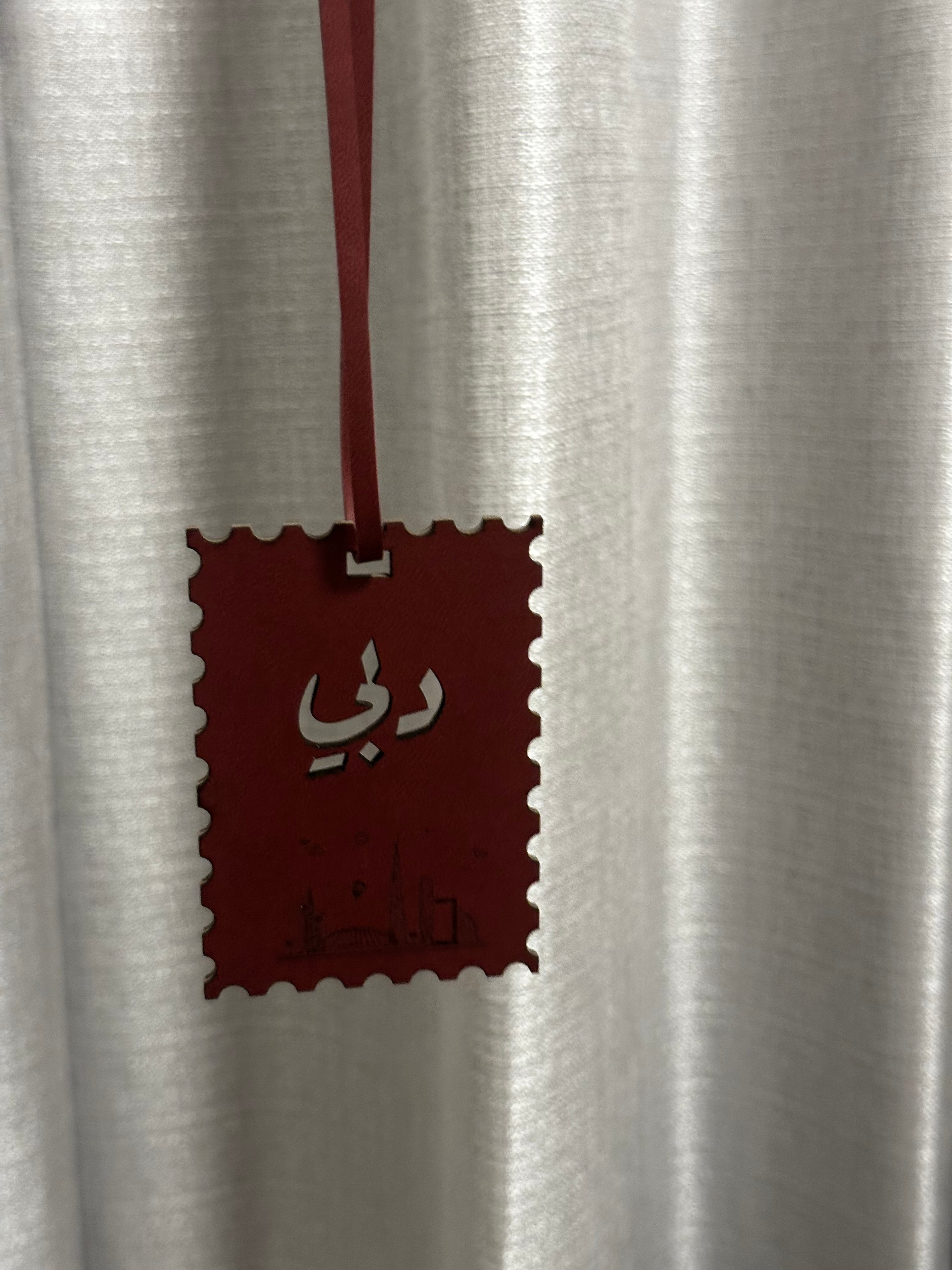 Red decorative tag with Arabic text on a white curtain background