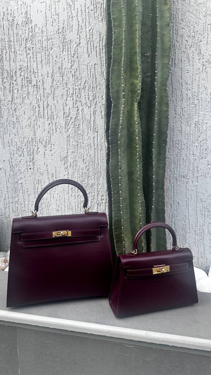Two burgundy handbags on a gray surface with a textured white wall and cactus in the background.
