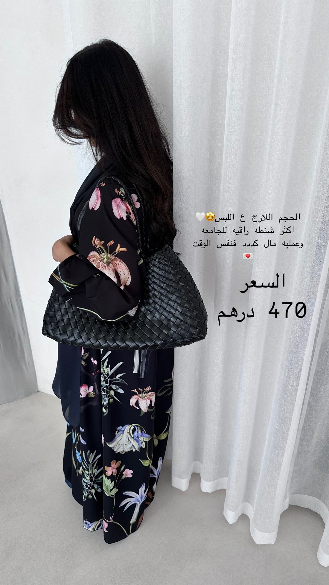 Woman wearing a floral dress with a black bag against a white curtain background