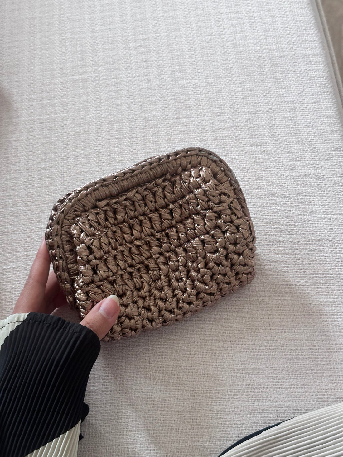 Hand holding a woven pouch on a light gray surface