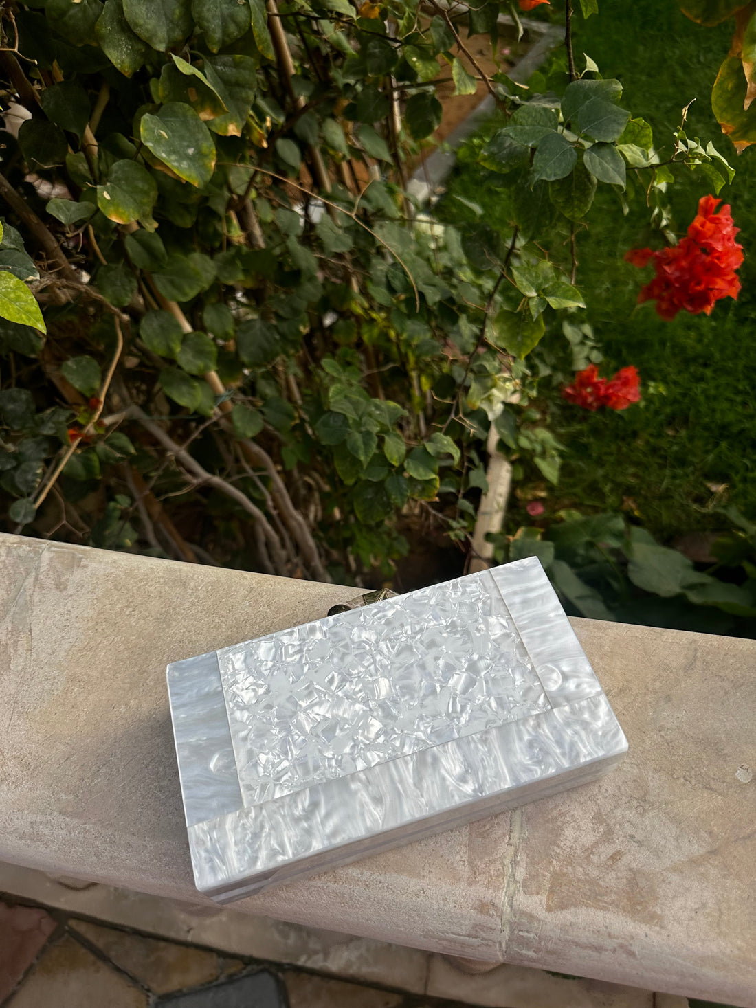 Silver block on a stone surface with greenery and red flowers in the background