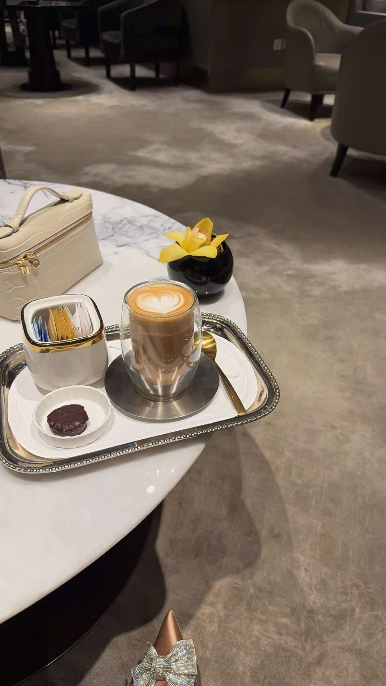 Cappuccino on a tray with a small flower and a bag in a cafe setting