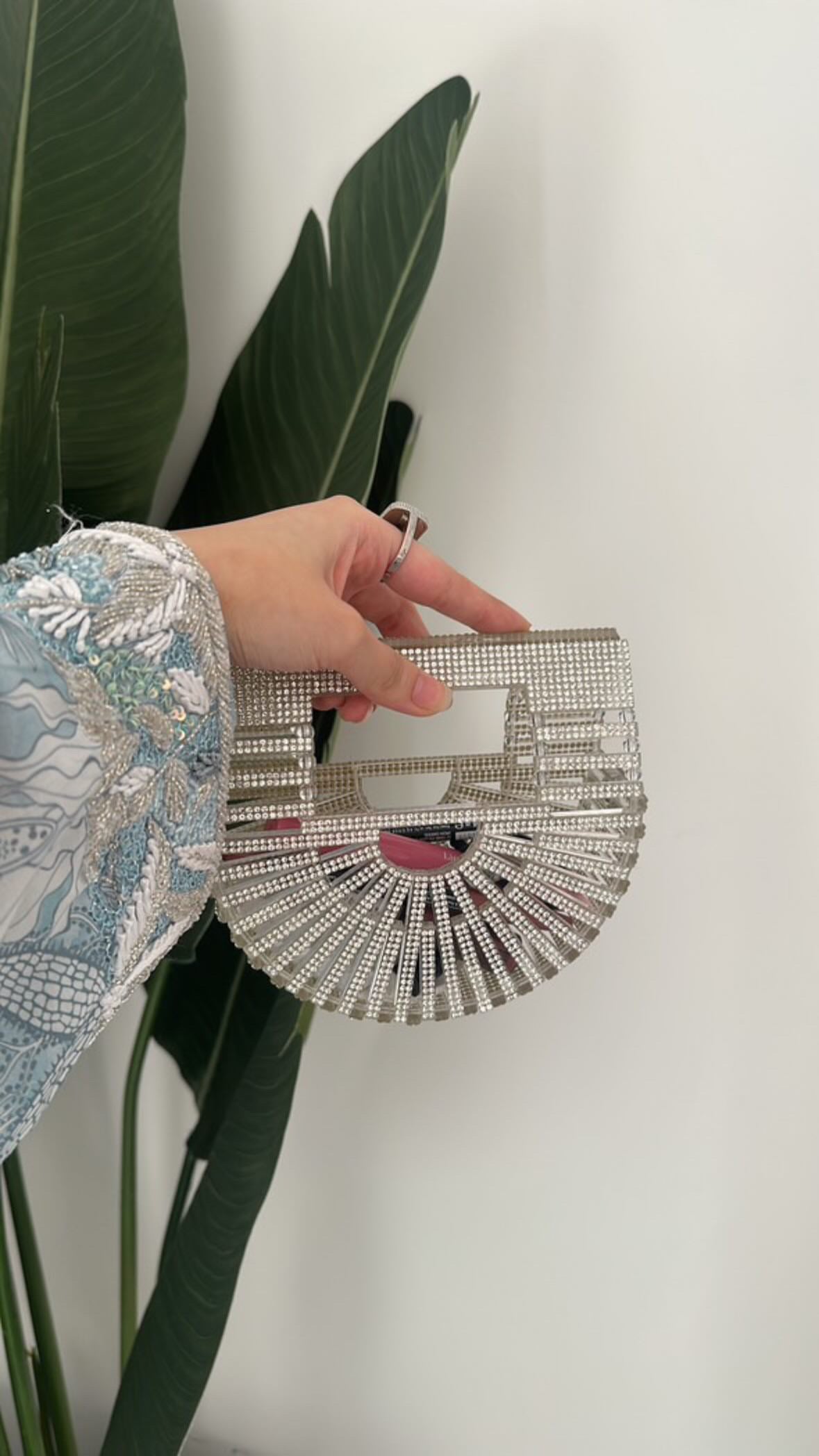 Hand holding a silver clutch with intricate design against a white background