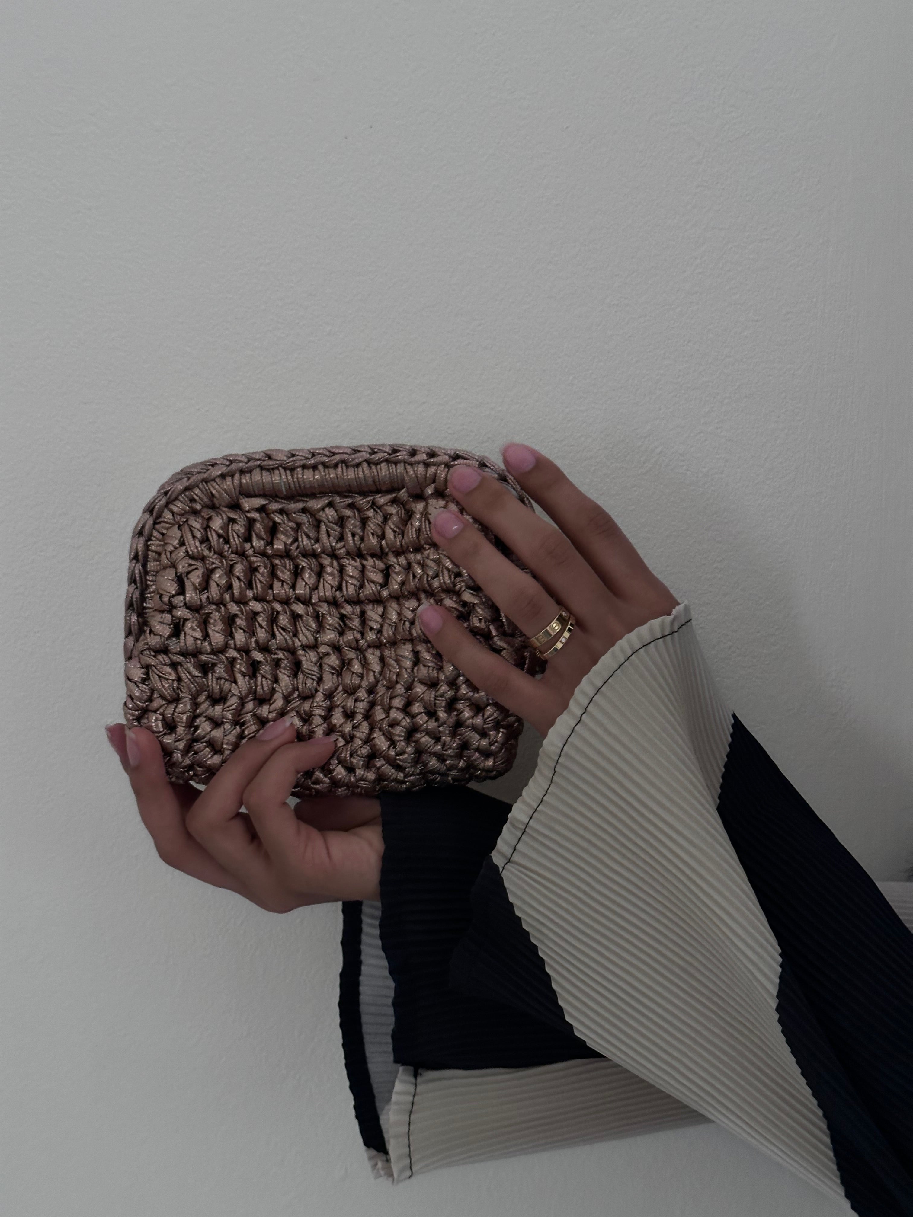 Hand holding a woven pouch against a plain background