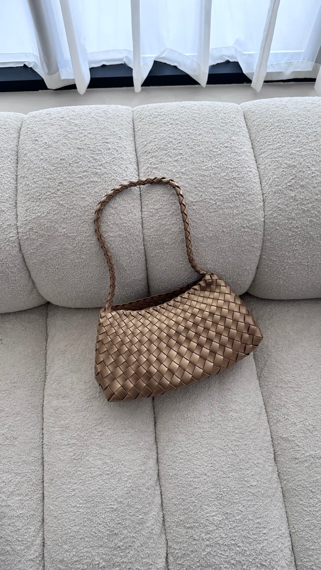 Woven handbag on a beige sofa with white curtains in the background