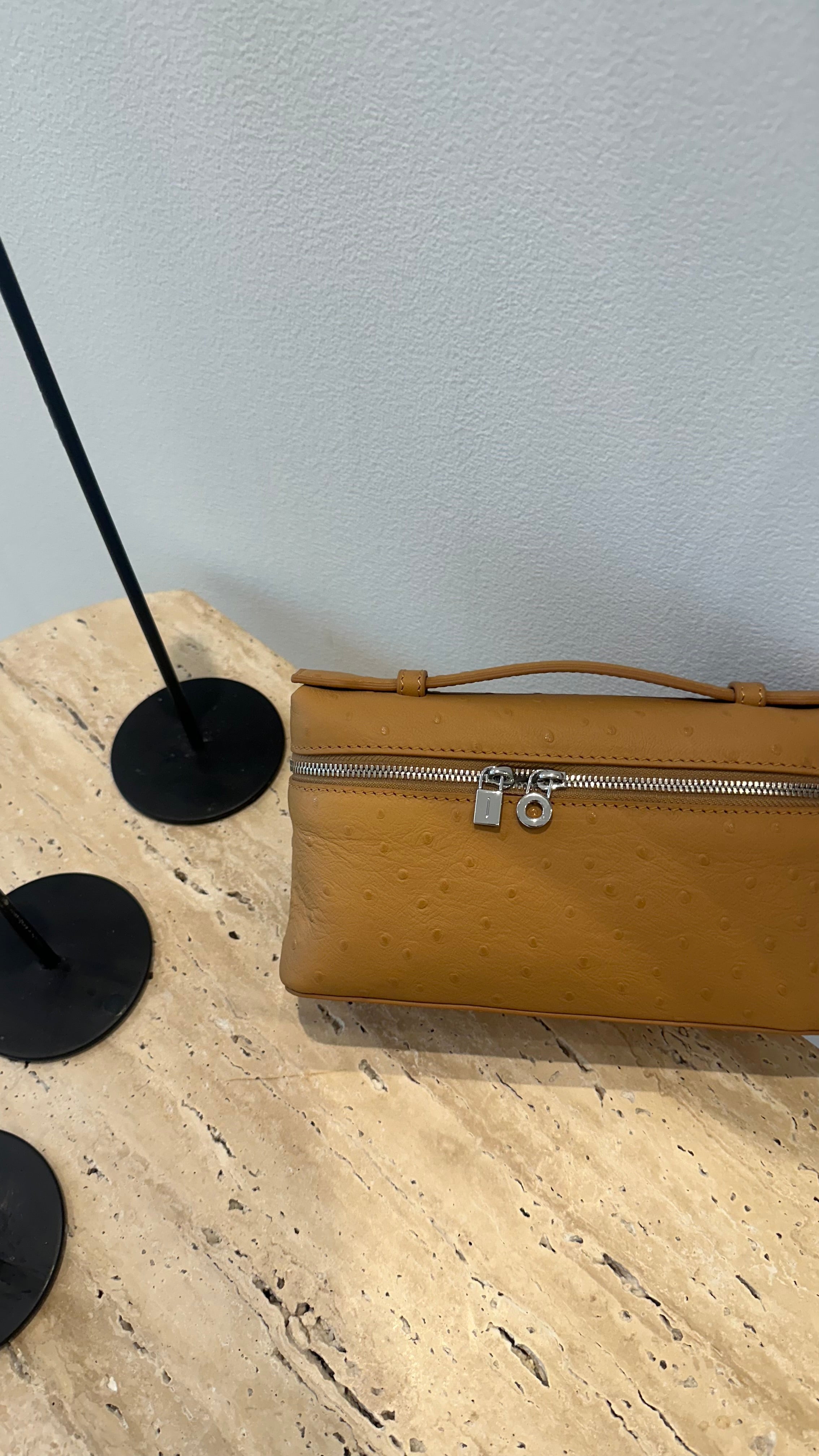 A brown leather handbag with a long strap, placed on a textured surface.
