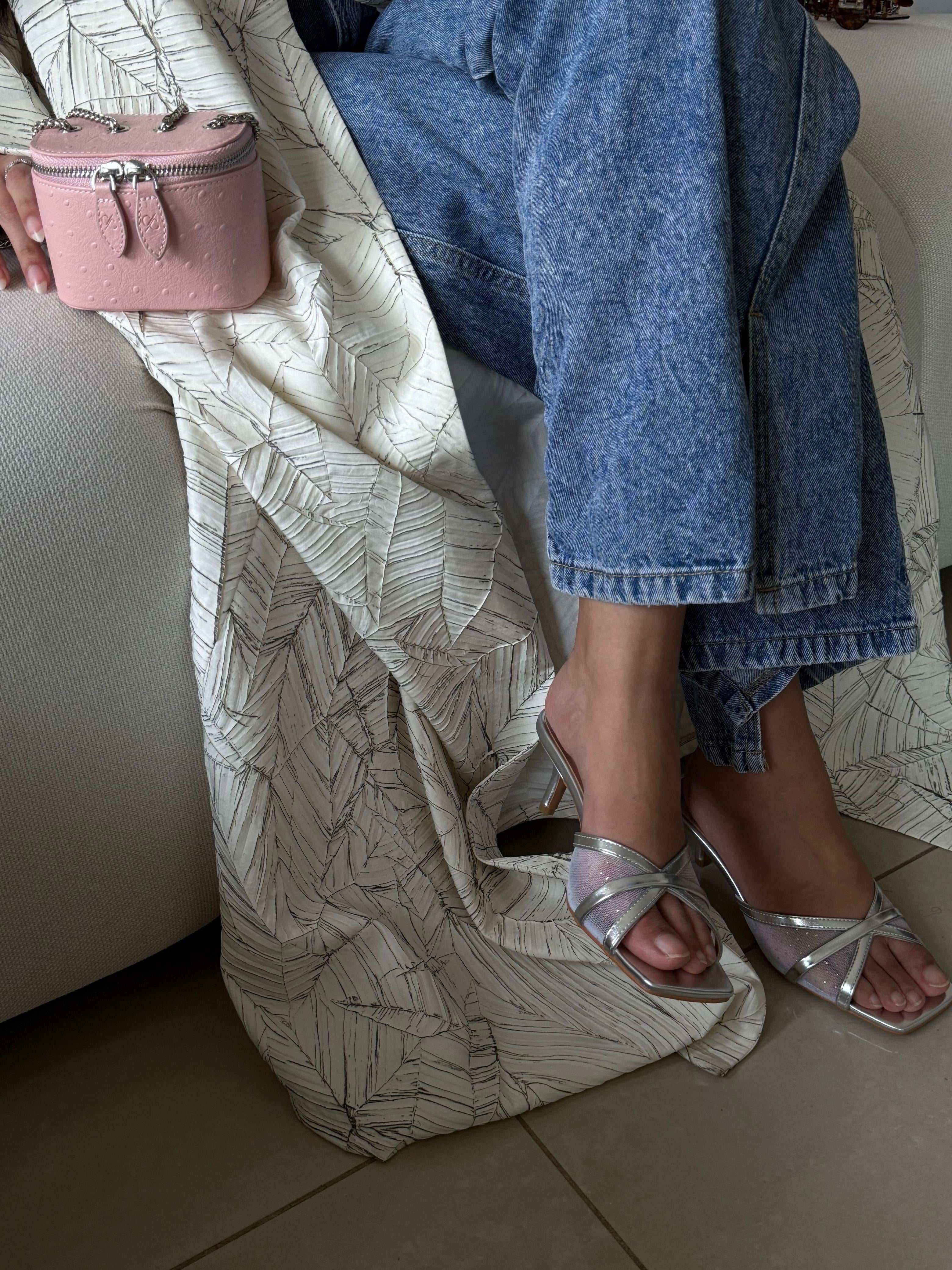 Person wearing blue jeans and silver sandals stepping out of a patterned bag on a light-colored couch.
