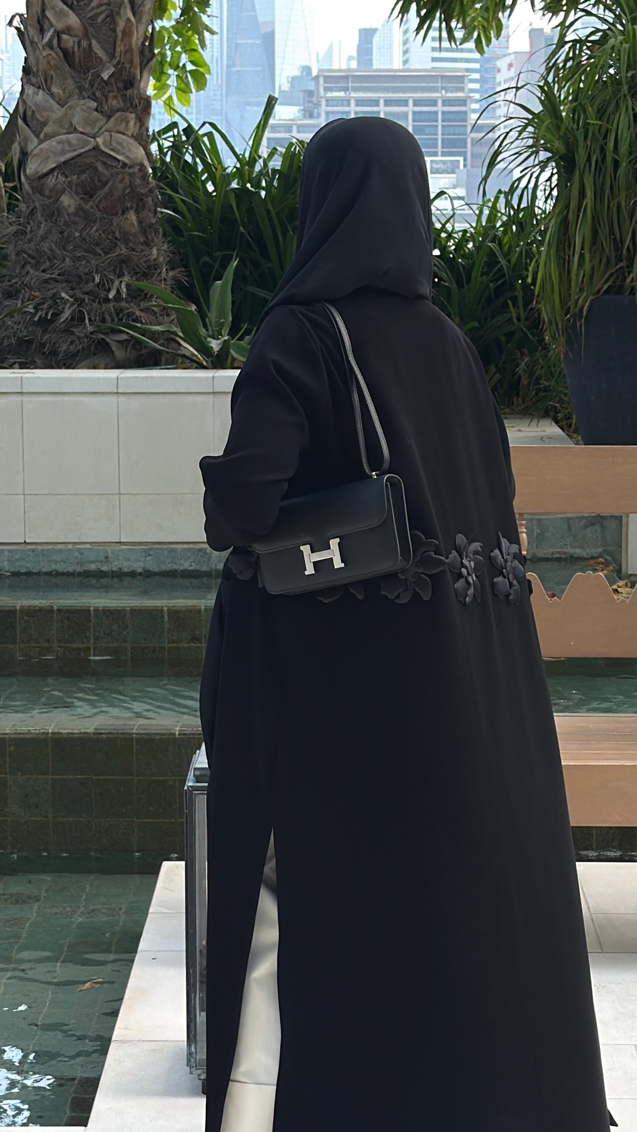 Person wearing a black abaya with a visible brand logo in an outdoor setting.