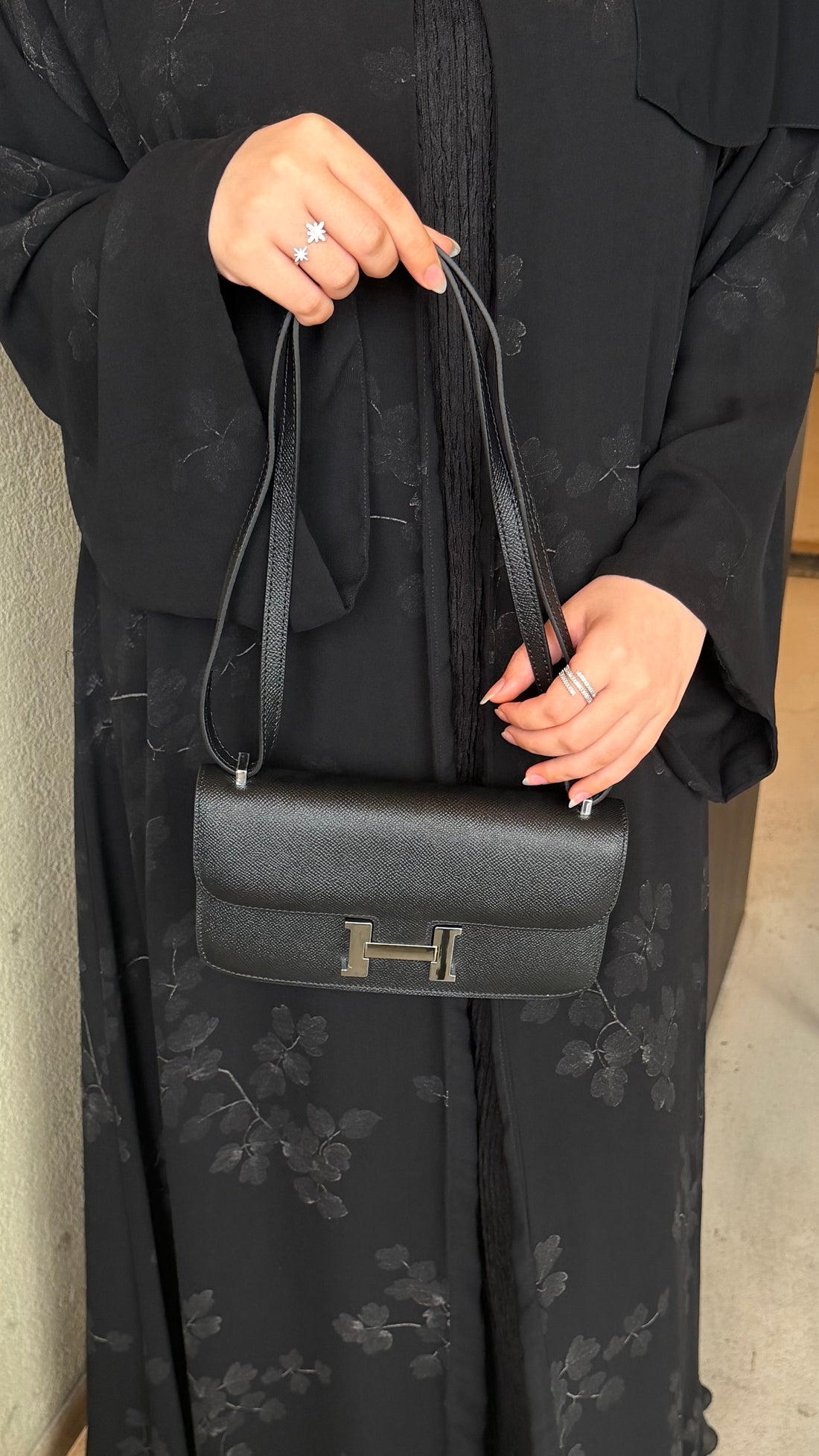 Two small ottomans with a black handbag, sunglasses, and a drink on top against a gray wall.
