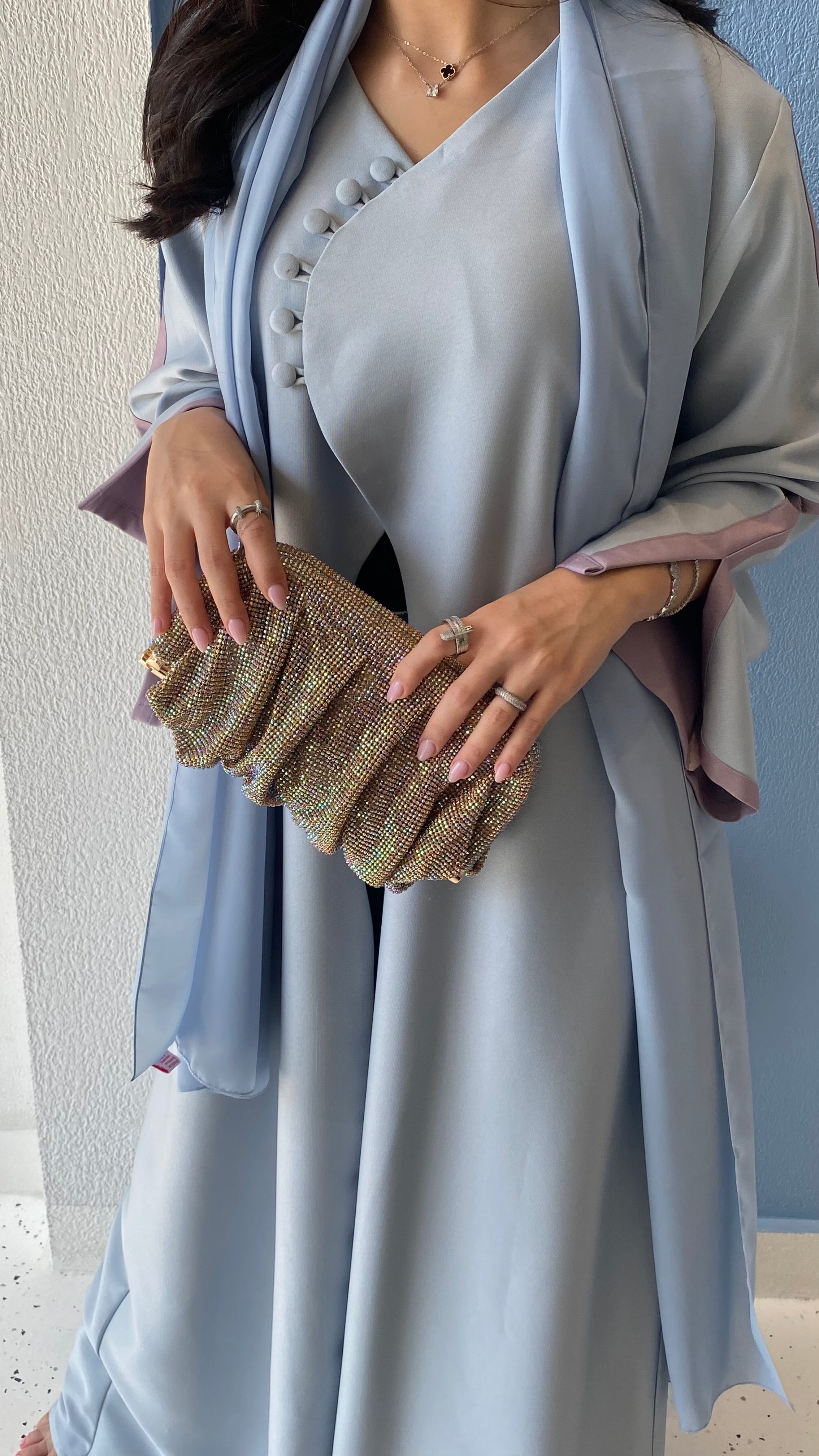 Woman holding a glittery clutch wearing a light blue dress with a matching shawl.