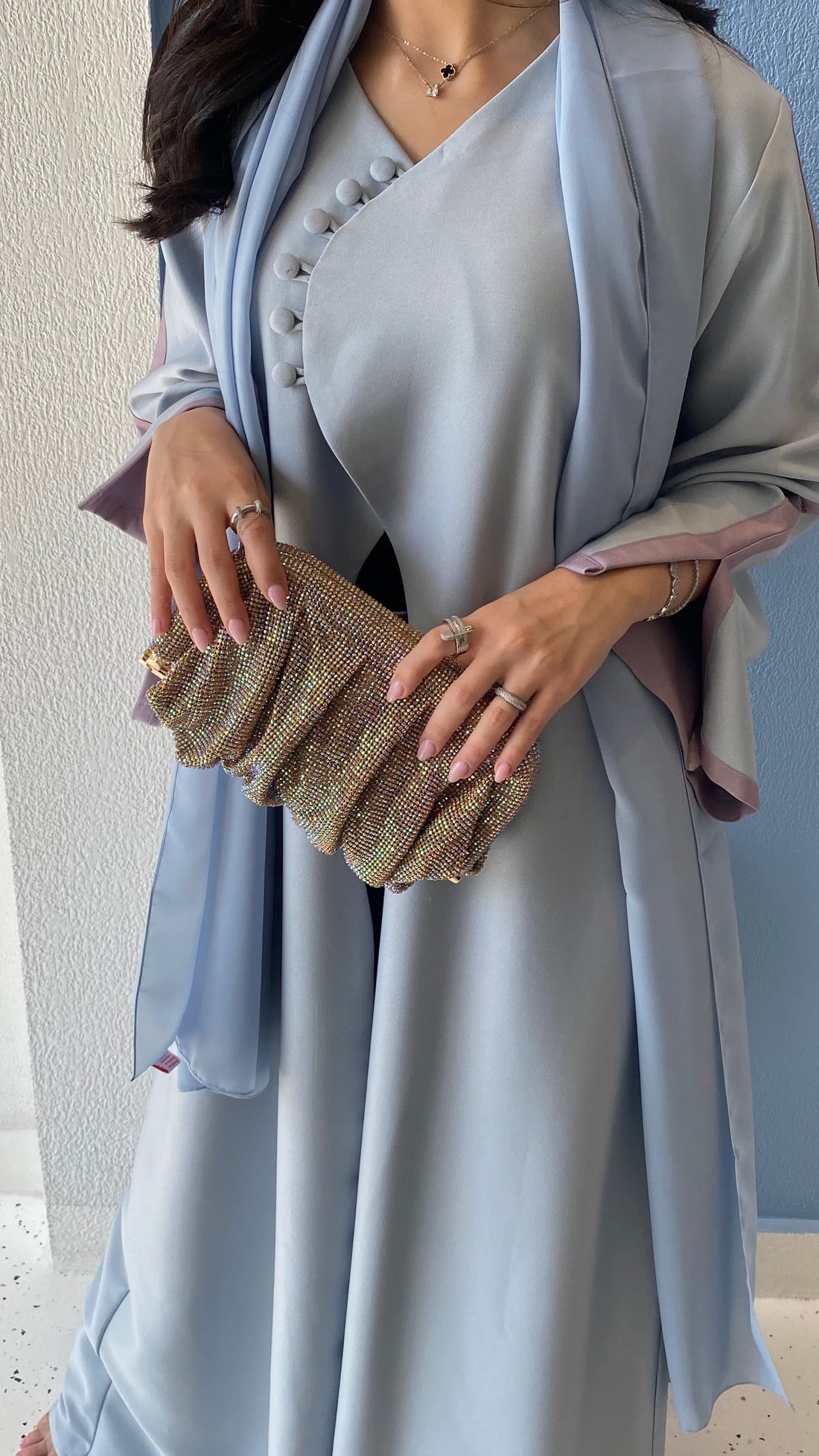 Woman holding a glittery clutch wearing a light blue dress with a matching shawl.