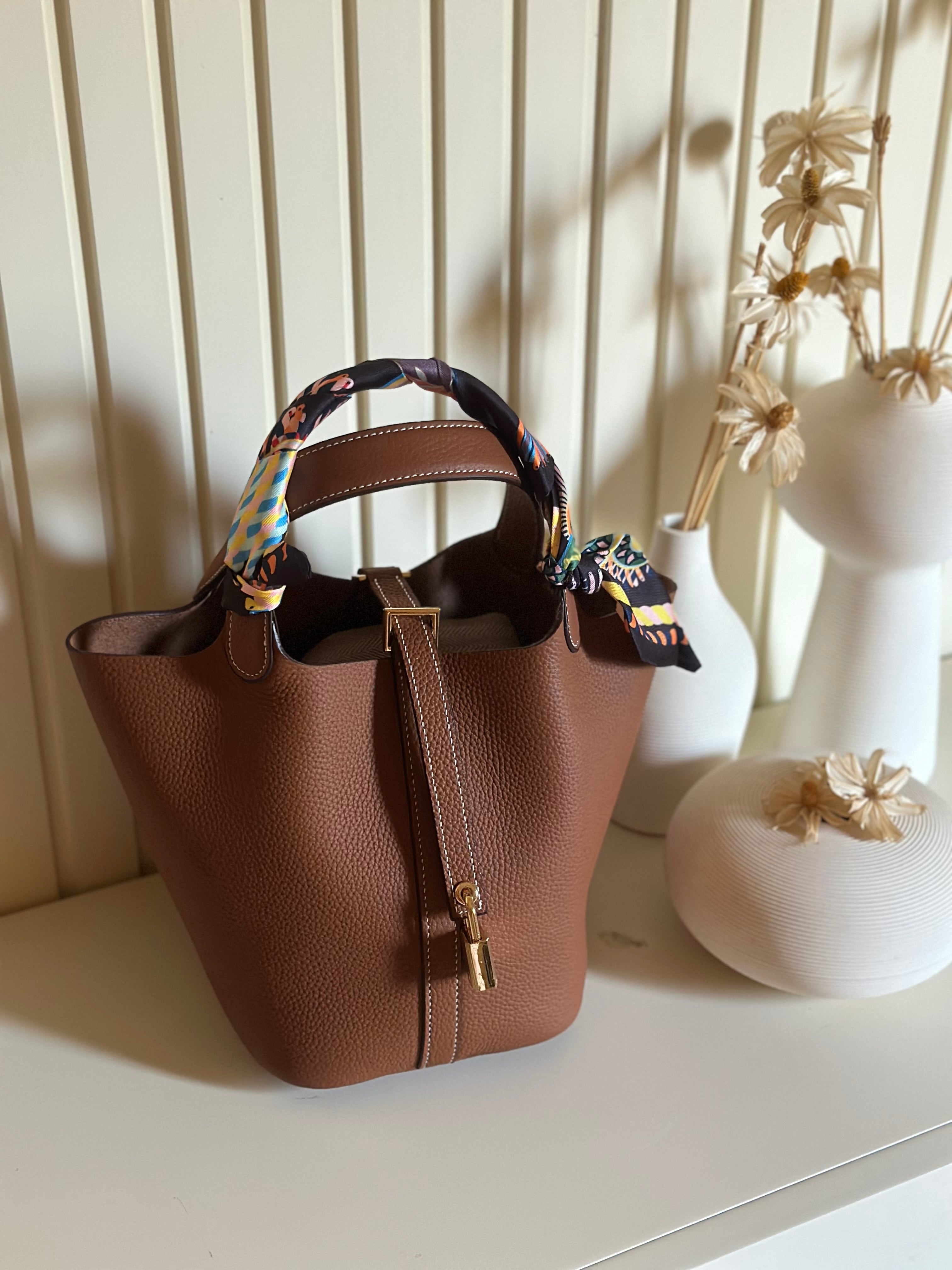 A brown handbag with a gold finish padlock and a multicolored strap placed on a white surface.