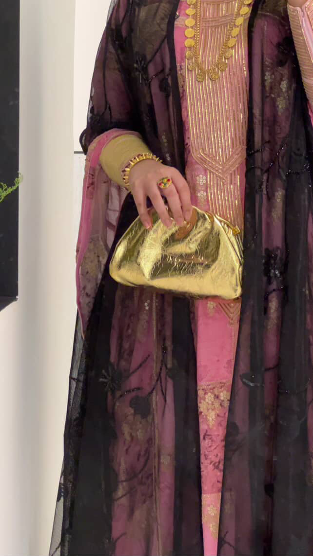 Person holding a gold clutch with a traditional outfit in the background