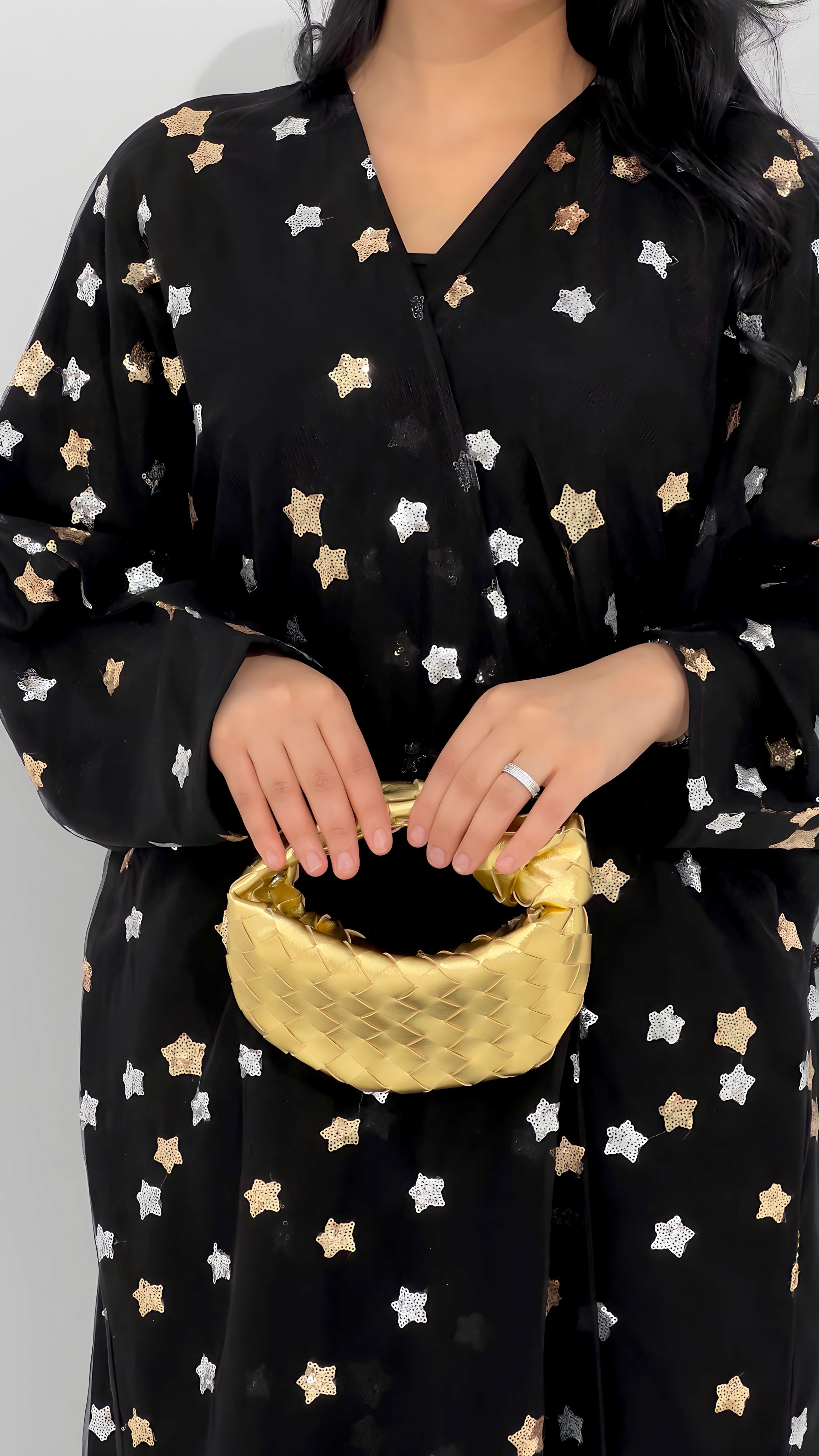 A person holding a small gold handbag with a chain strap.