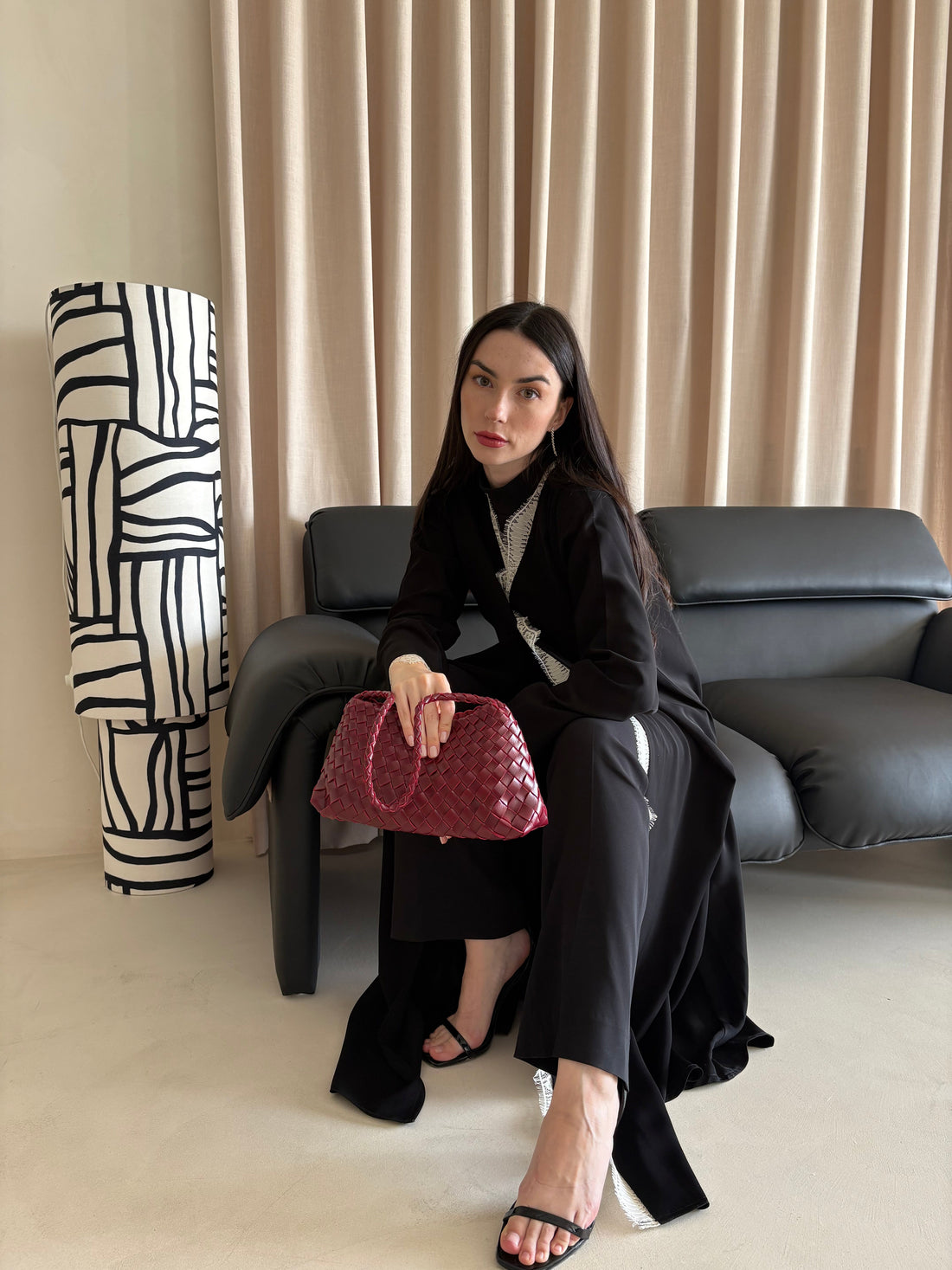 Woman holding a pink handbag in a room with a black sofa and patterned floor lamp.