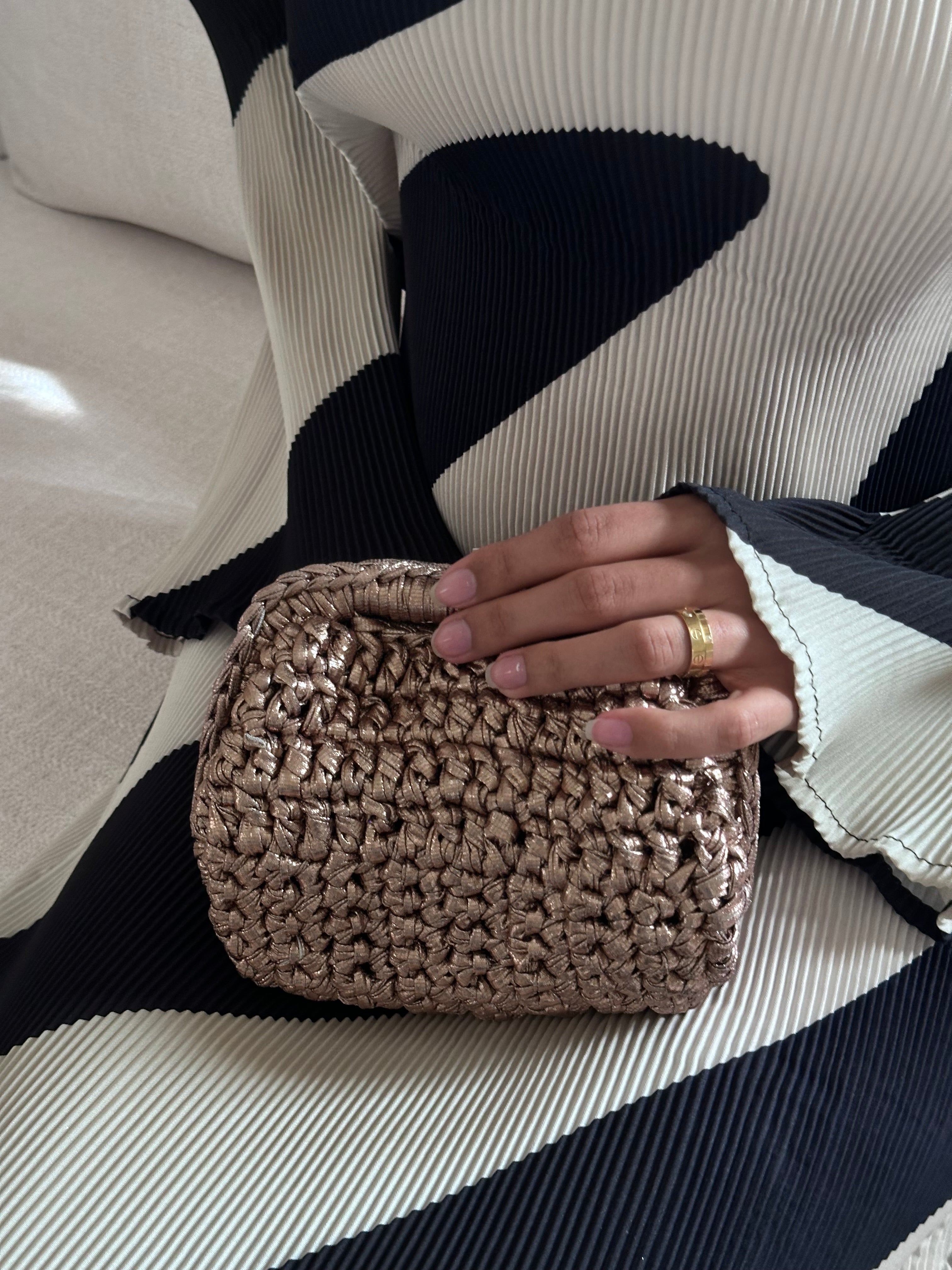 Hand holding a woven clutch bag with a striped background