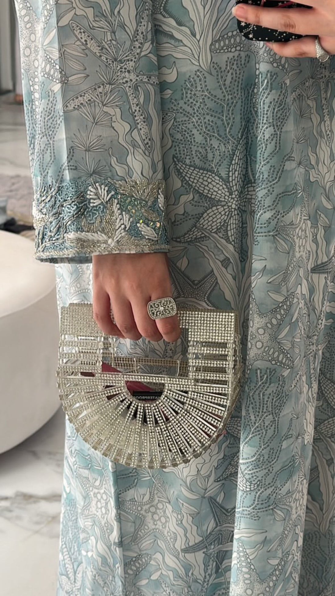 Person wearing a patterned outfit holding a silver handbag.