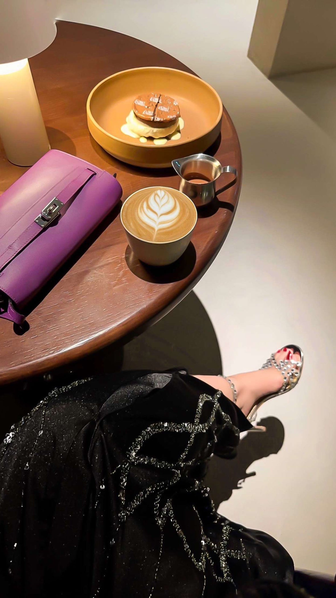 Café setting with a cup of coffee, purple bag, and decorative bowl on a wooden table.
