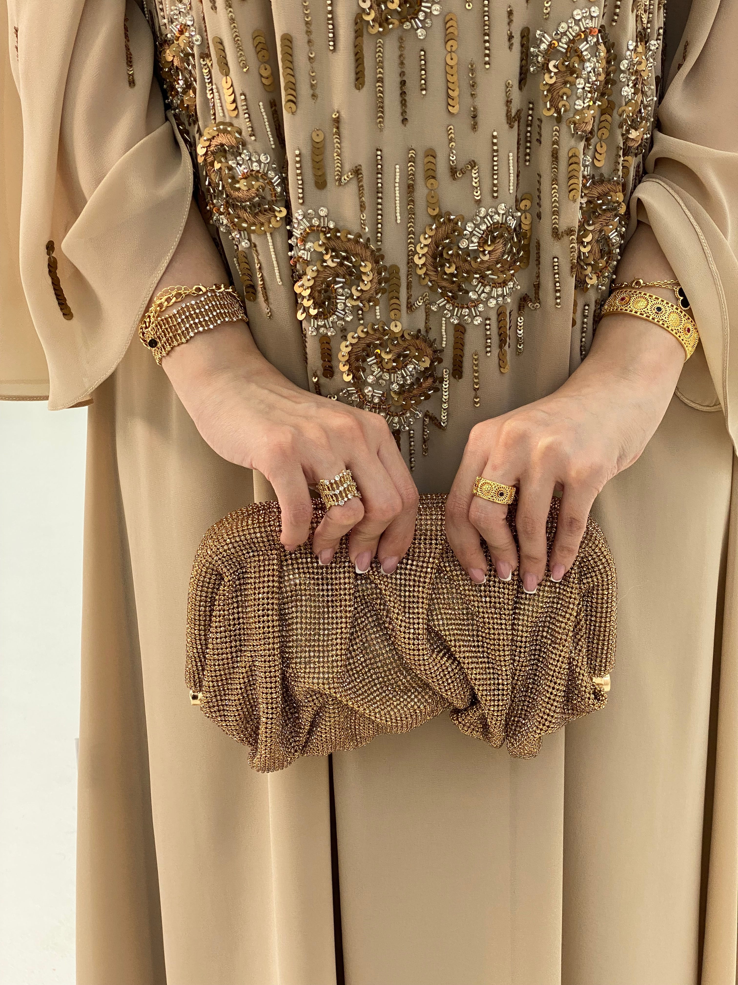 Close-up of a person holding a gold clutch with intricate designs, wearing a matching outfit.