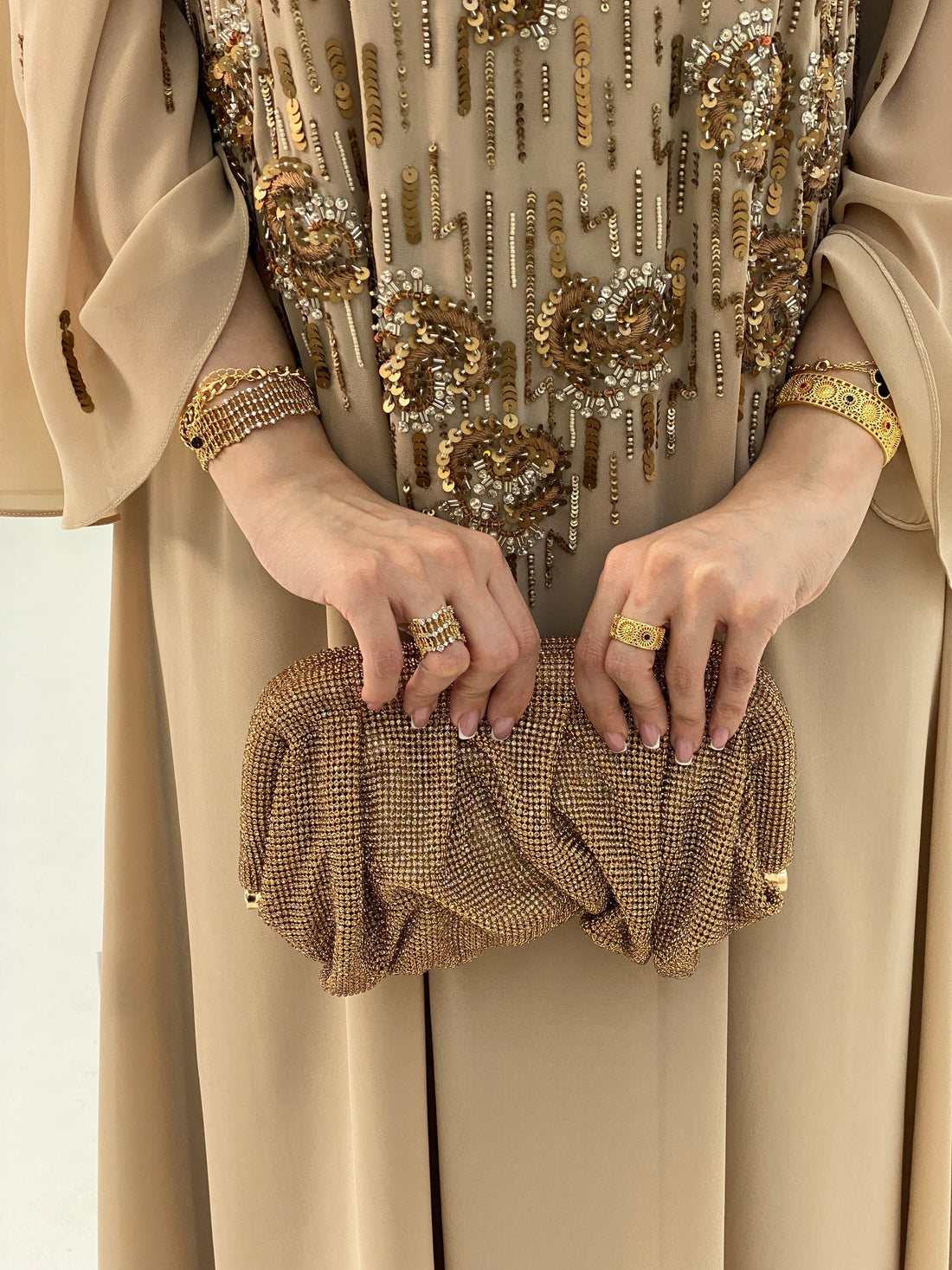 Close-up of a person holding a gold clutch with intricate designs, wearing a matching outfit.