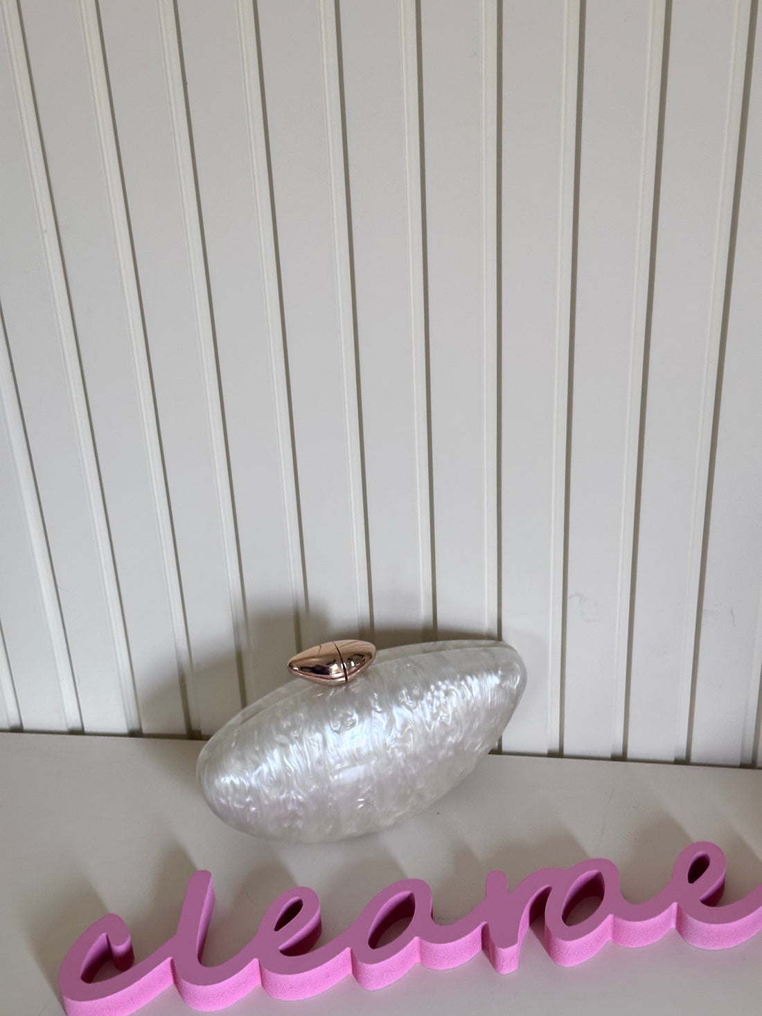 Silver clutch bag on a white surface with a pink 'eleven' sign in the foreground against a white paneled wall.