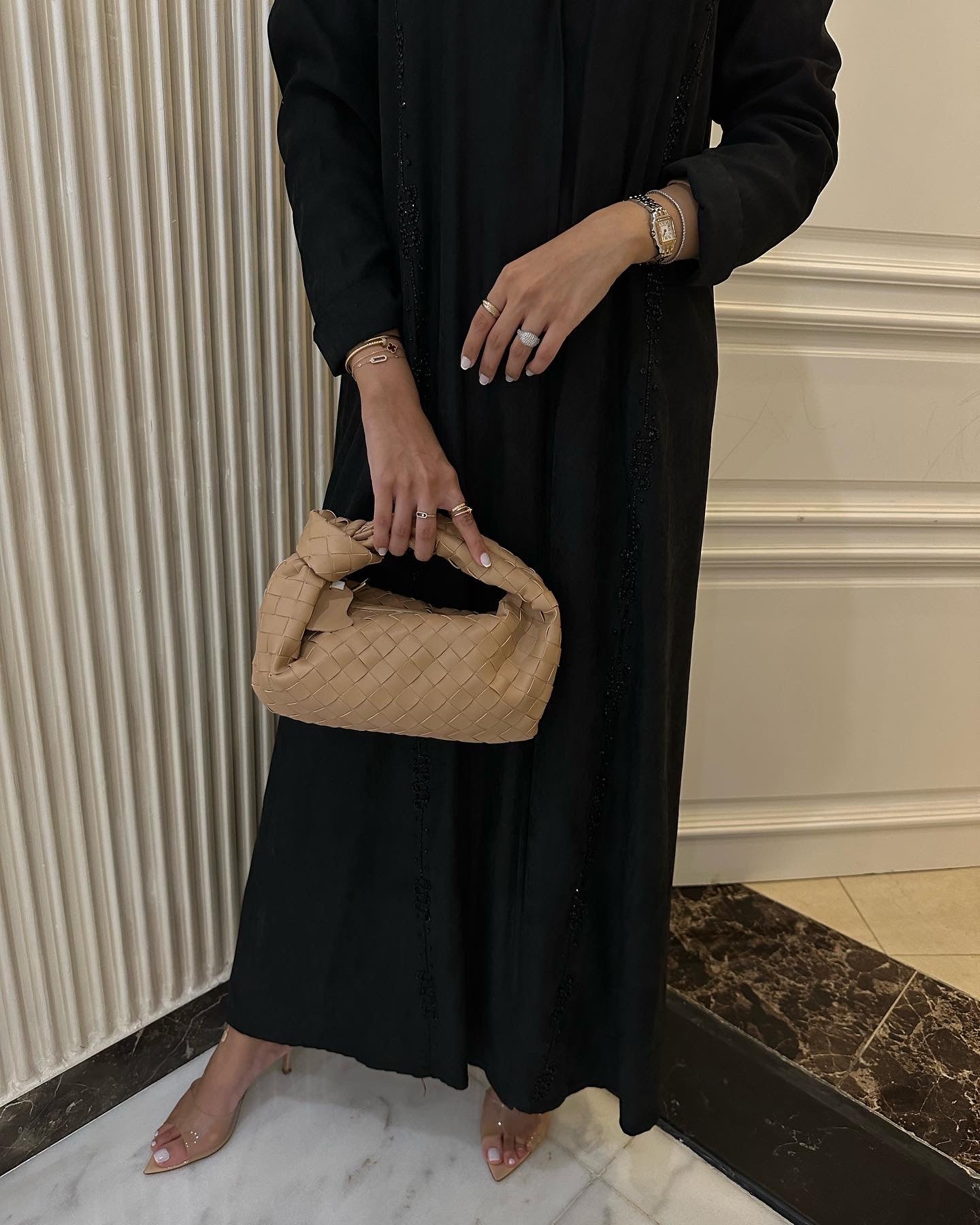 Person holding a beige handbag wearing a black outfit indoors.