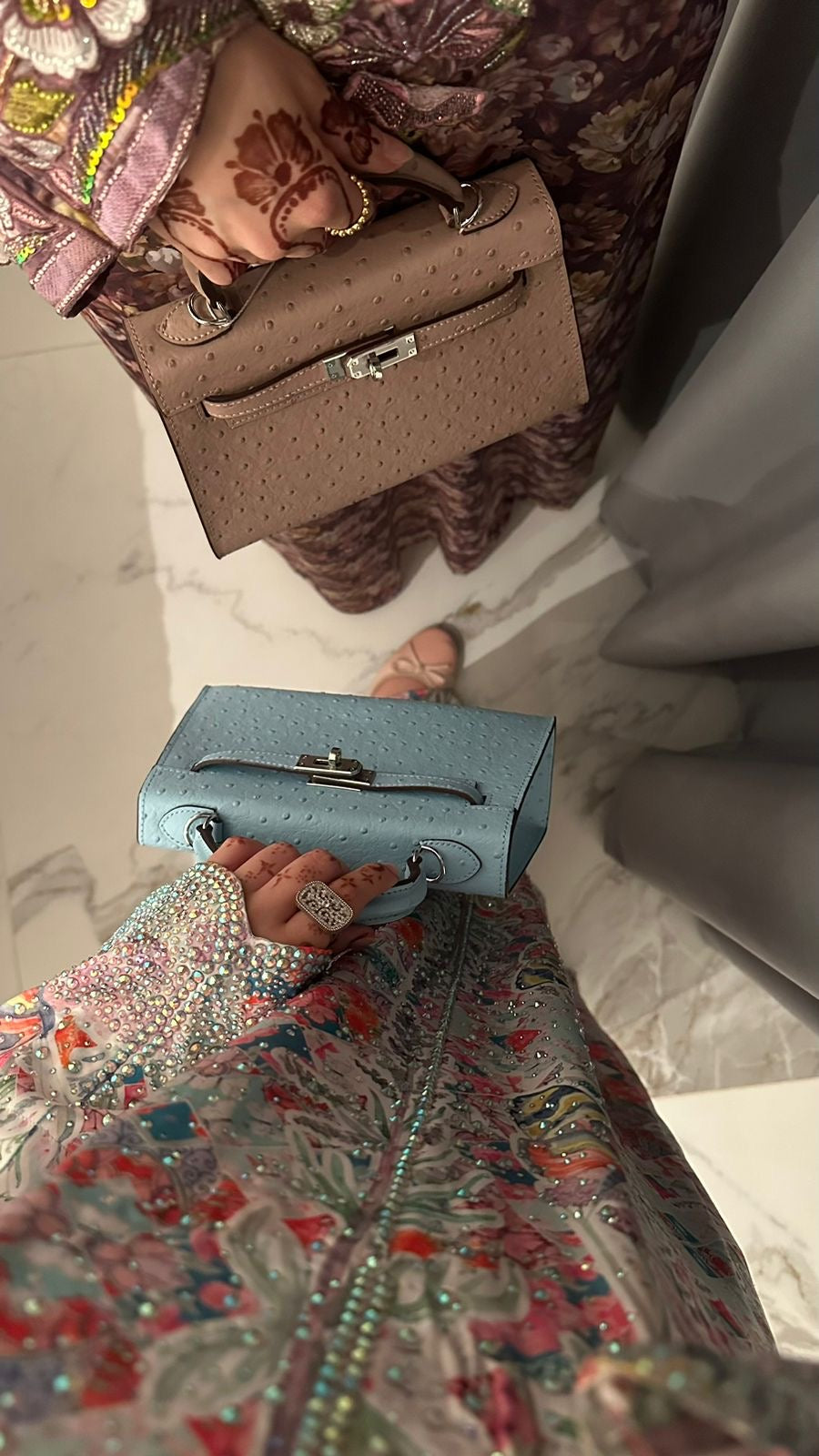 Person holding a blue handbag with a floral dress and jewelry.