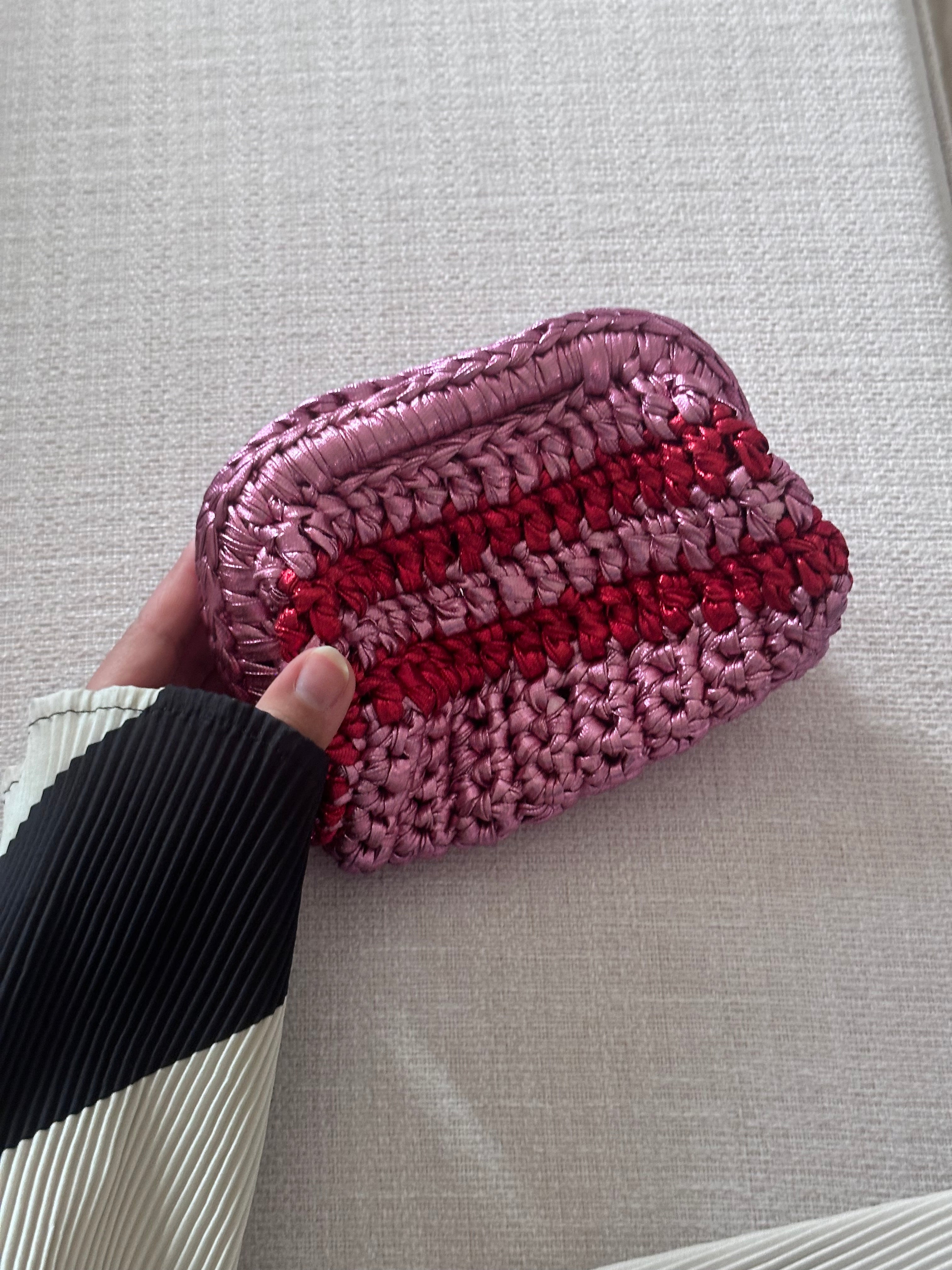 Pink and red striped woven pouch held by a hand on a light gray surface