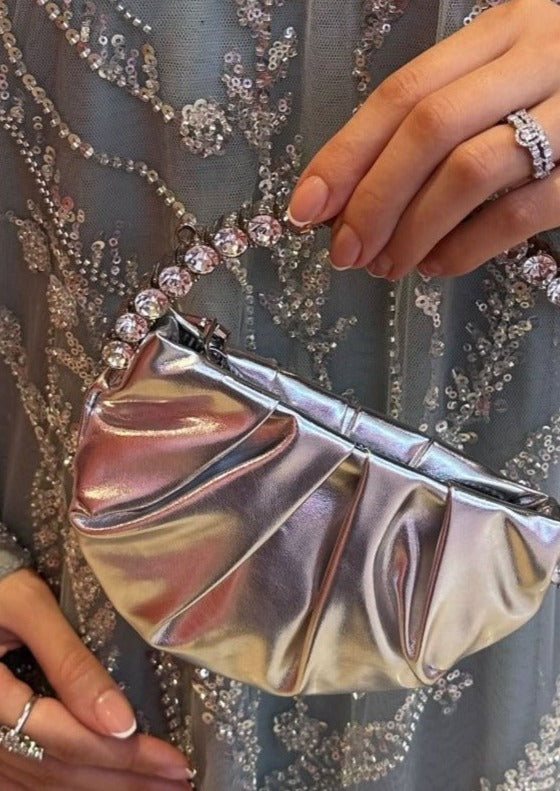 A person holding a small, silver, round handbag with a long chain.