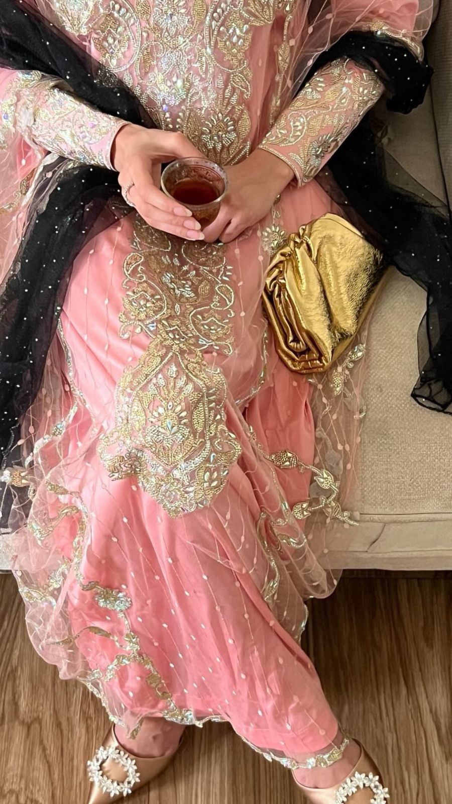 Person wearing a pink traditional outfit with gold embroidery, holding a small container.