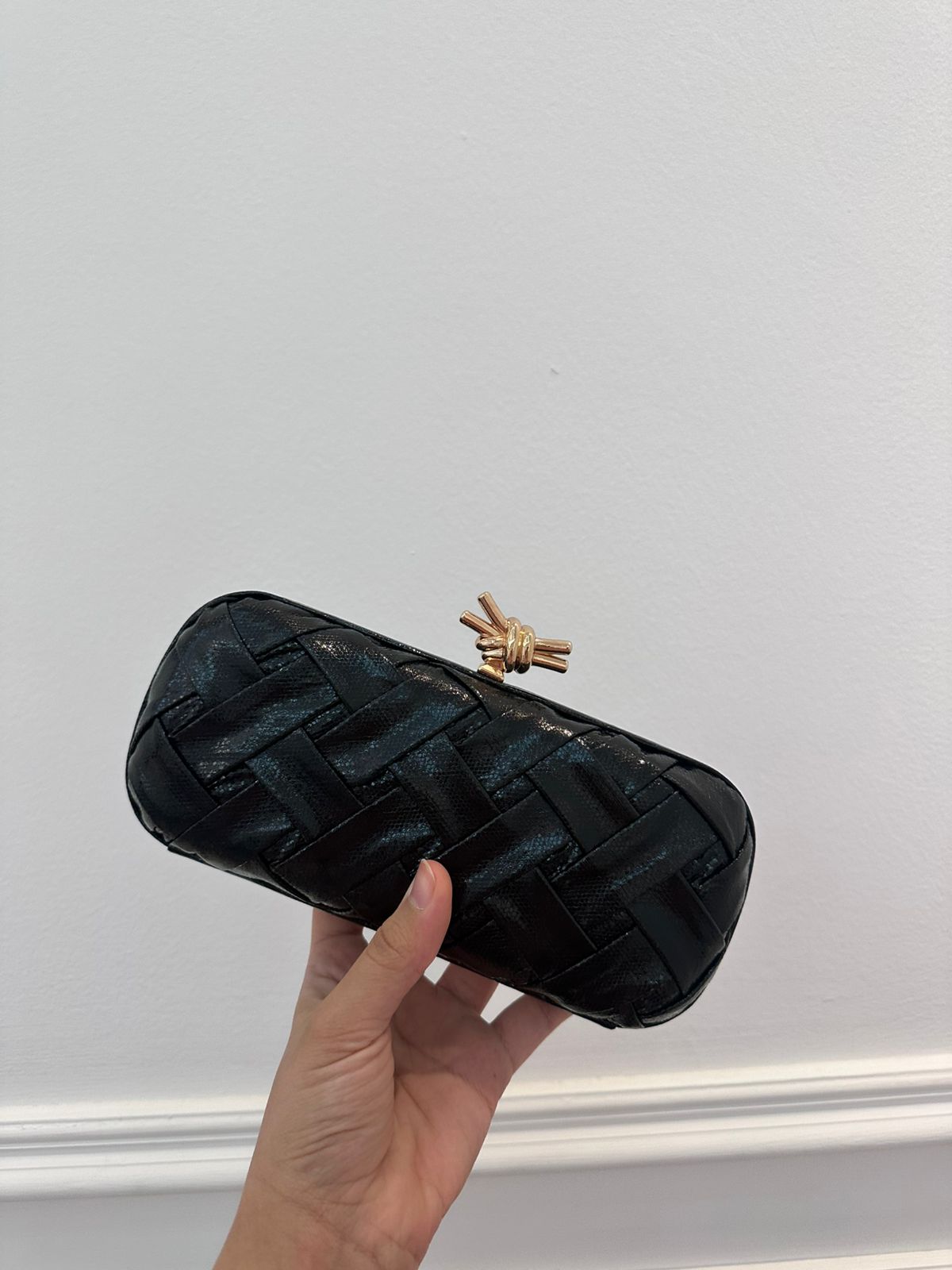 Black textured clutch held by a hand against a light gray background