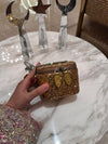 Gold embellished clutch held by a hand on a marble surface with decorative items in the background.