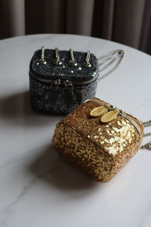 Two glittery handbags, one gold and one black, on a marble surface.