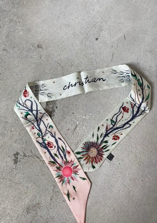 A clear silk scarf with a floral pattern, including shades of pink and green, displayed on a surface.