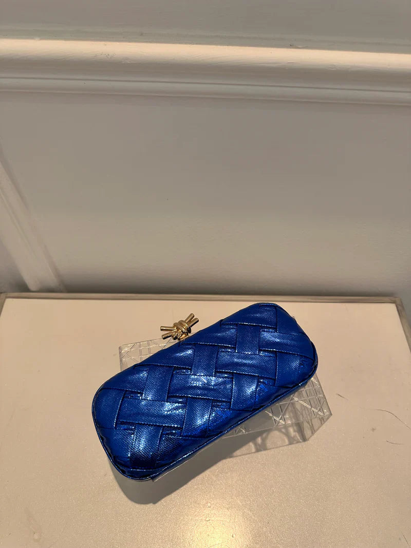 Blue woven clutch bag on a light-colored surface with a neutral background