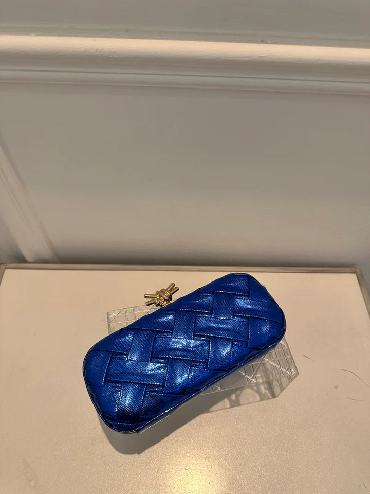 Blue woven clutch bag on a light-colored surface with a neutral background