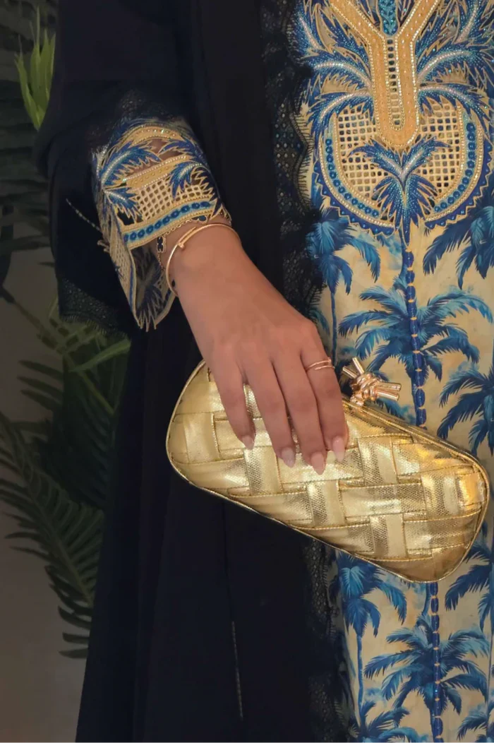 Hand holding a gold clutch with a patterned background