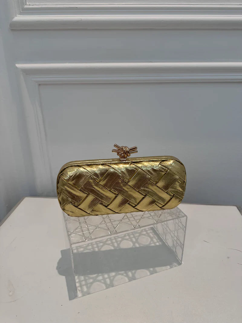 Gold woven clutch bag on a clear stand against a white background