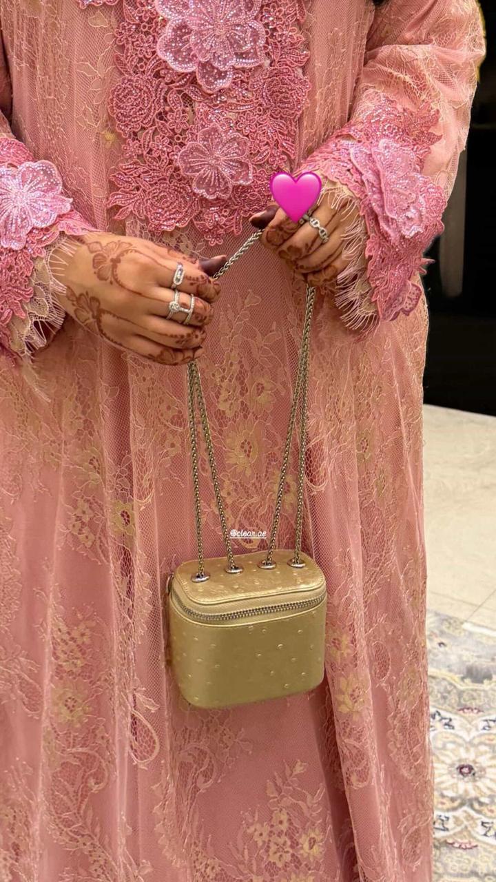 Person wearing a pink embroidered outfit holding a small green handbag with a pink heart charm.