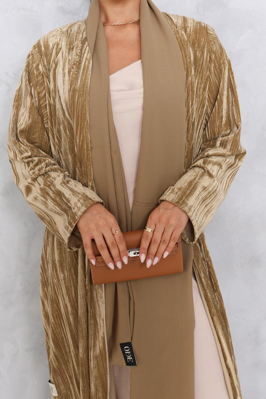 Person wearing a long, patterned beige coat holding a brown clutch against a white background