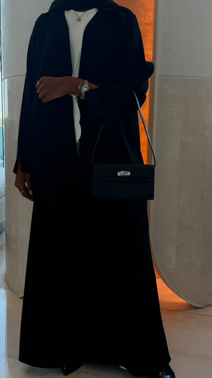 Black clutch bag worn crossbody with abaya outfit