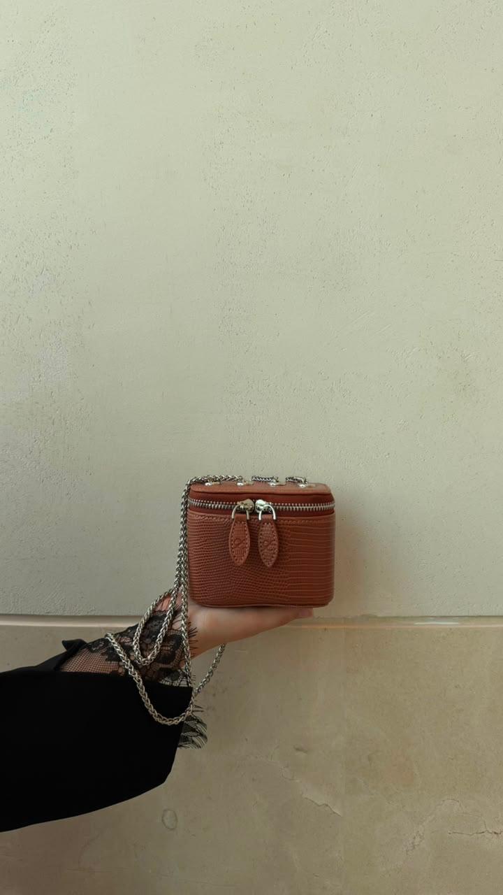 Mini Vanity Chain Bag Brown held by chain strap by hand with black lace sleeve against light blue wall front view